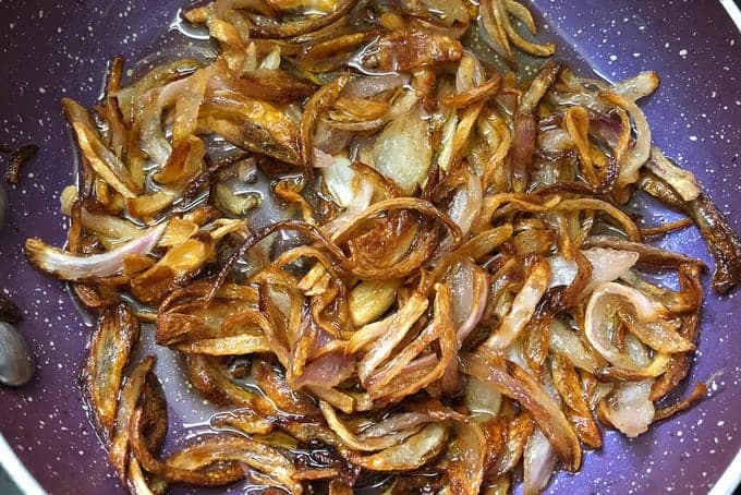 Heat ghee for tempering in a pan. Add sliced onion and fry until browned. Pour the tempering over the chicken.